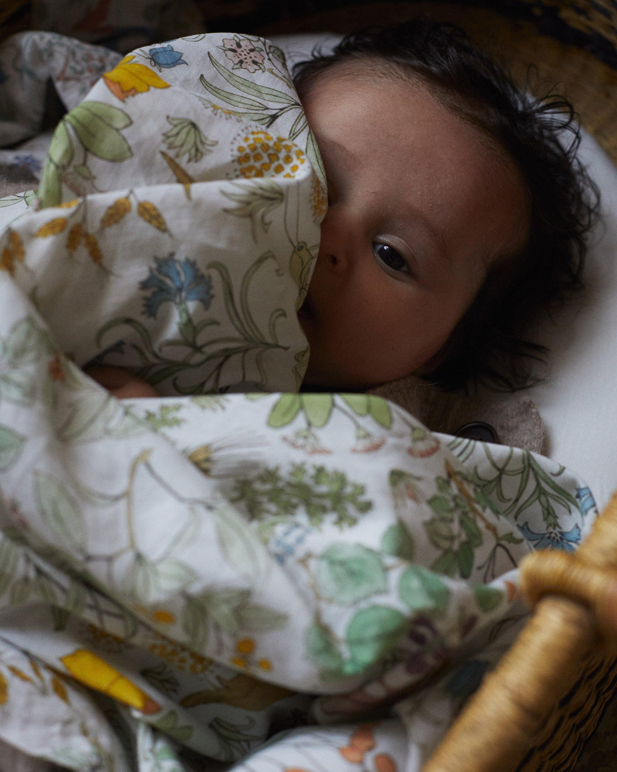 Cute baby girl peeking out over an organic muslin blanket with a traditional Voysey design