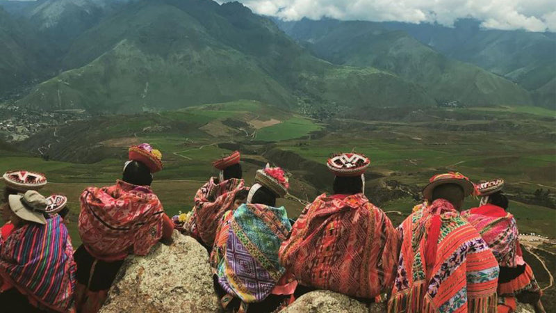 Female artisans sit on a mountain in Peru wearing brightly coloured, traditional dress.