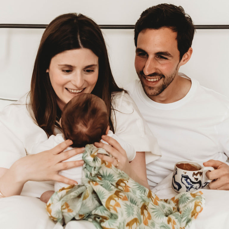 New parents smiling with newborn baby, with V&A animal print muslin