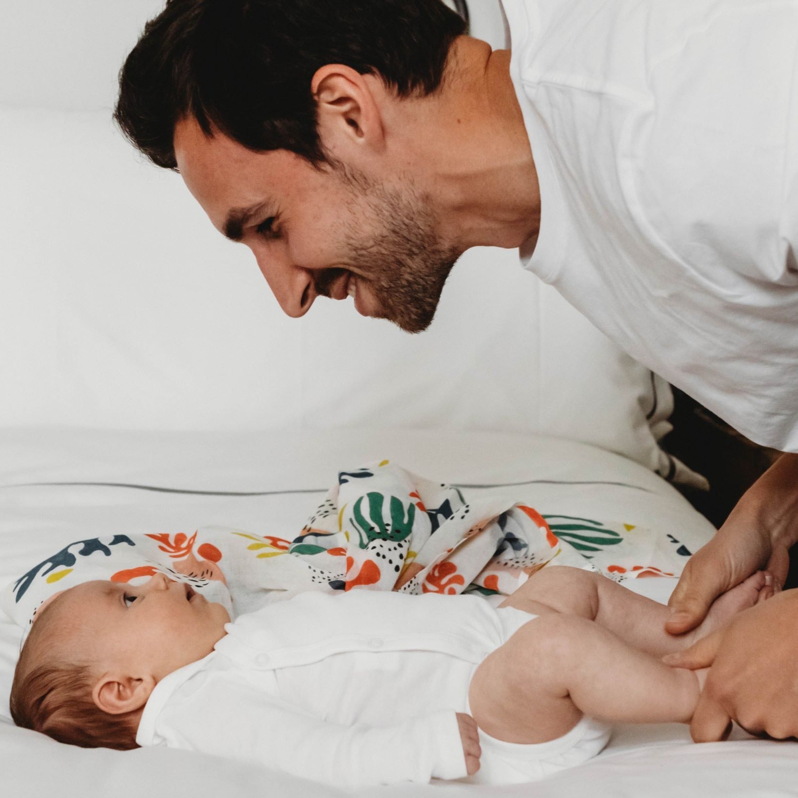 New dad smiles at newborn baby girl next to colourful organic cotton muslin 